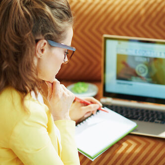 young woman with textbook using online school on laptop female smla student at computer taking notes