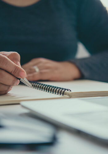 The hand of a man holding a pen and taking notes in a notebook. student writing in notebook at smla